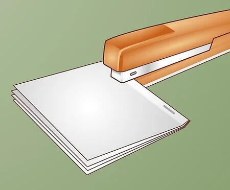 a stapler is stapling along the spine of a booklet zine